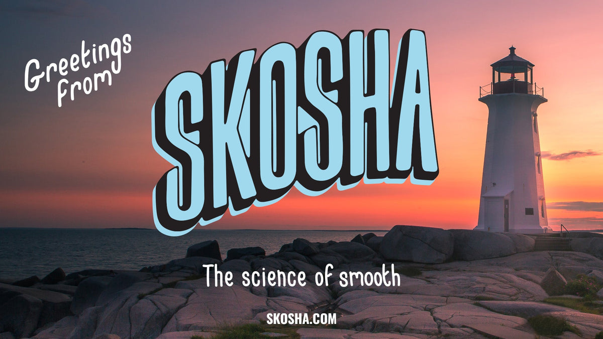 A stylized sunset seascape with a white lighthouse on rocky shoreline, overlaid with large decorative text reading 'SKOSHA' and smaller text 'Greetings From' and 'The science of smooth', plus 'SKOSHA.COM' at the bottom.